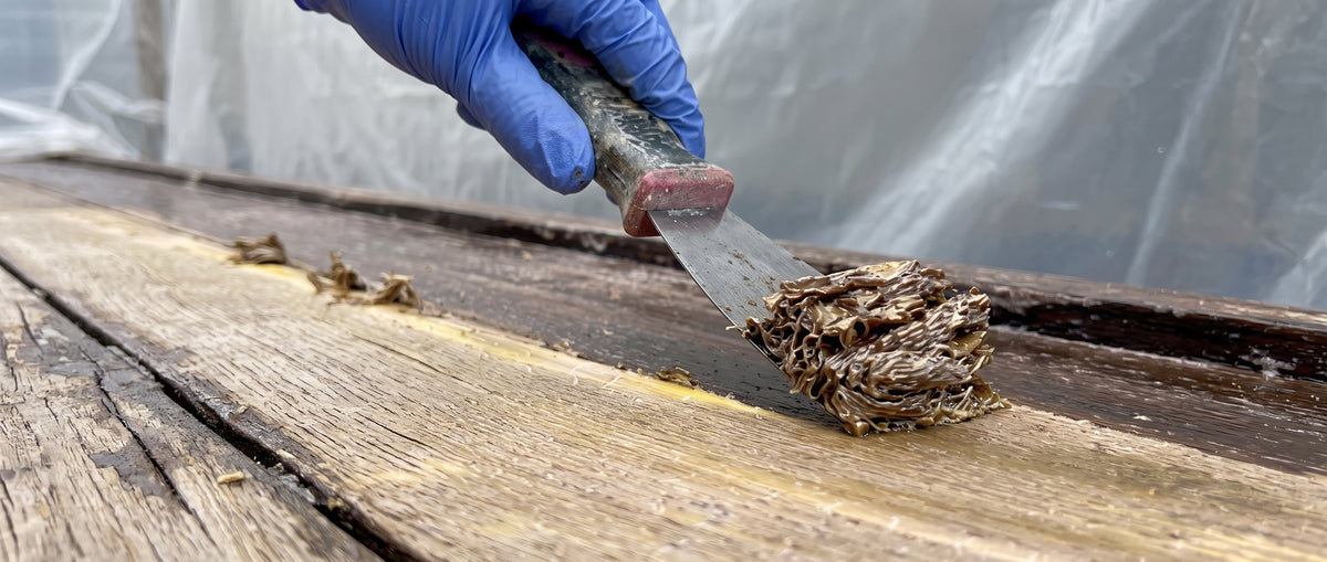 A scraper lifting a long ribbon of old paint off a table top